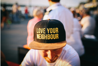 Man wearing a black, flat brim baseball cap that says "Love Your Neighbor" in yellow text