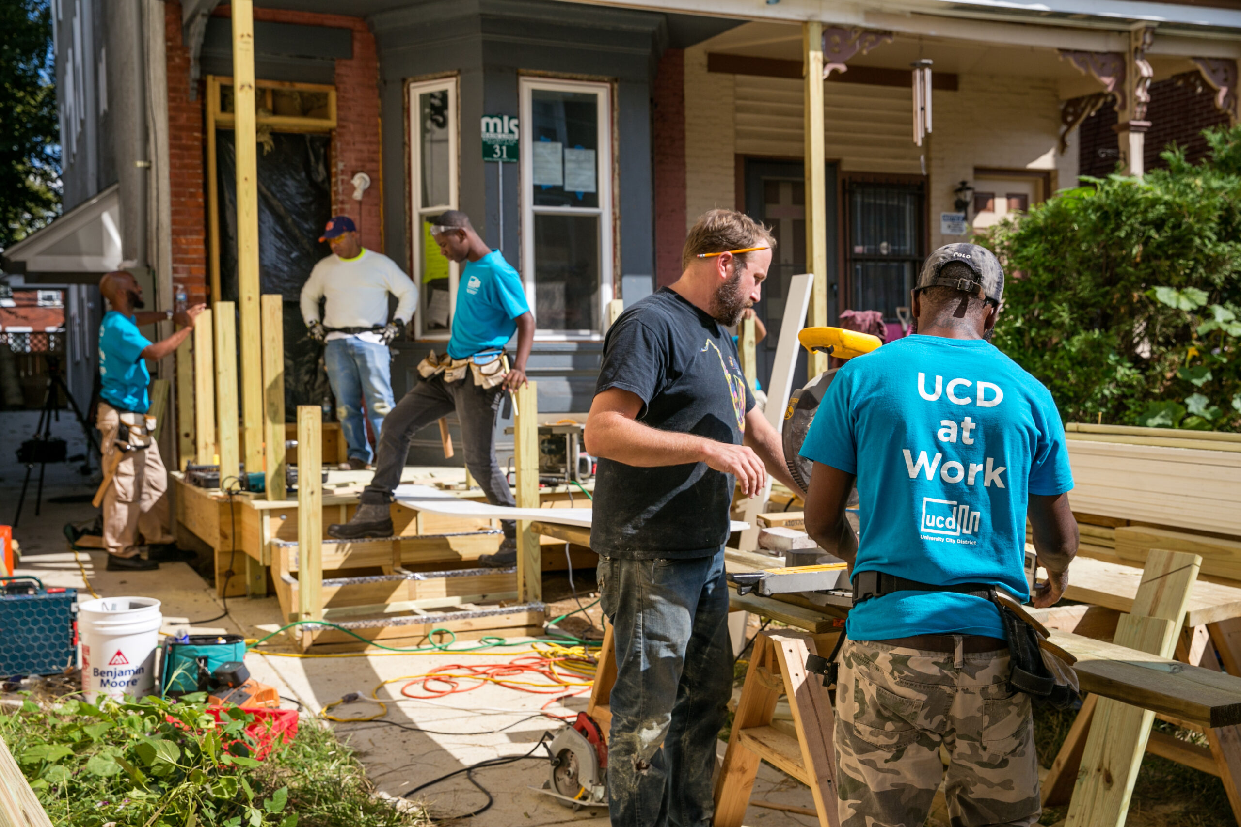 University City District team members building a porch on Preston Street, with tools, wood materials, and active construction work visible.