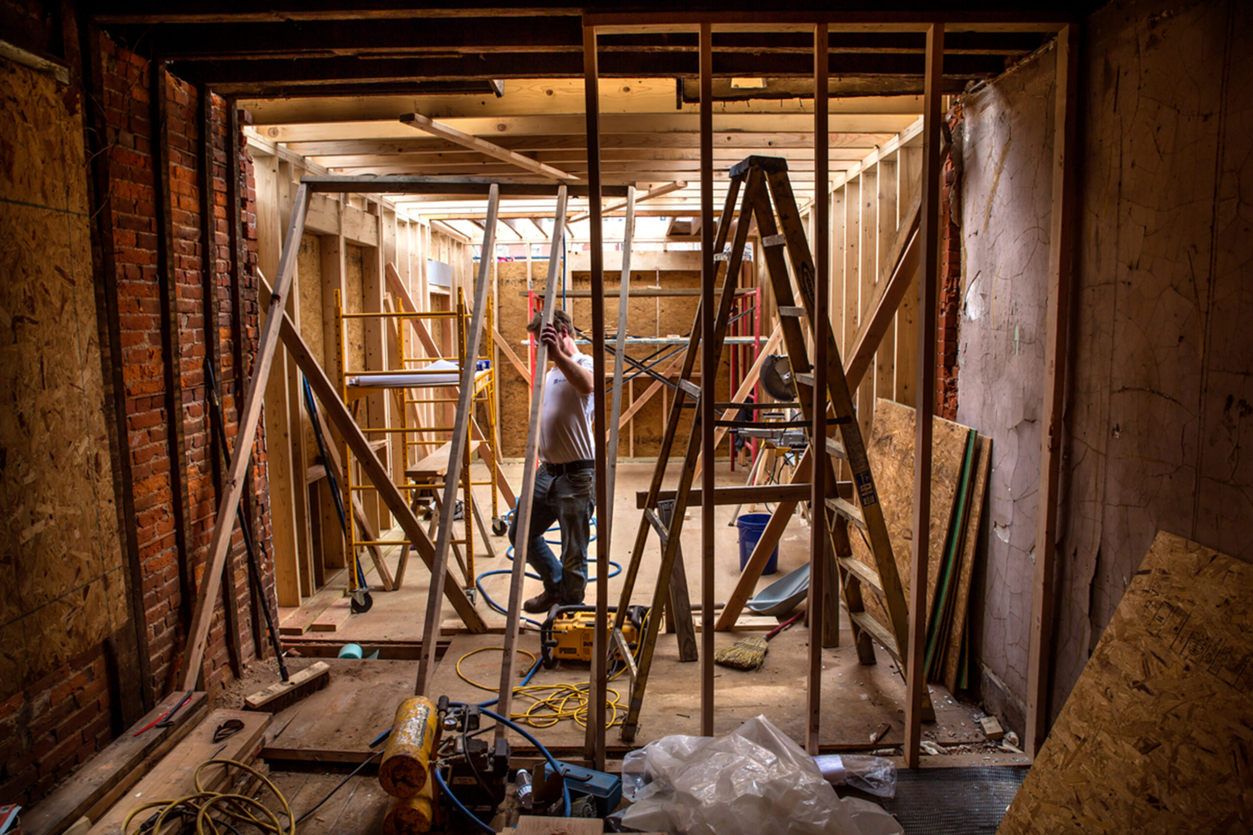 Construction worker inside a rowhouse with wooden framing and construction tools during a renovation project.