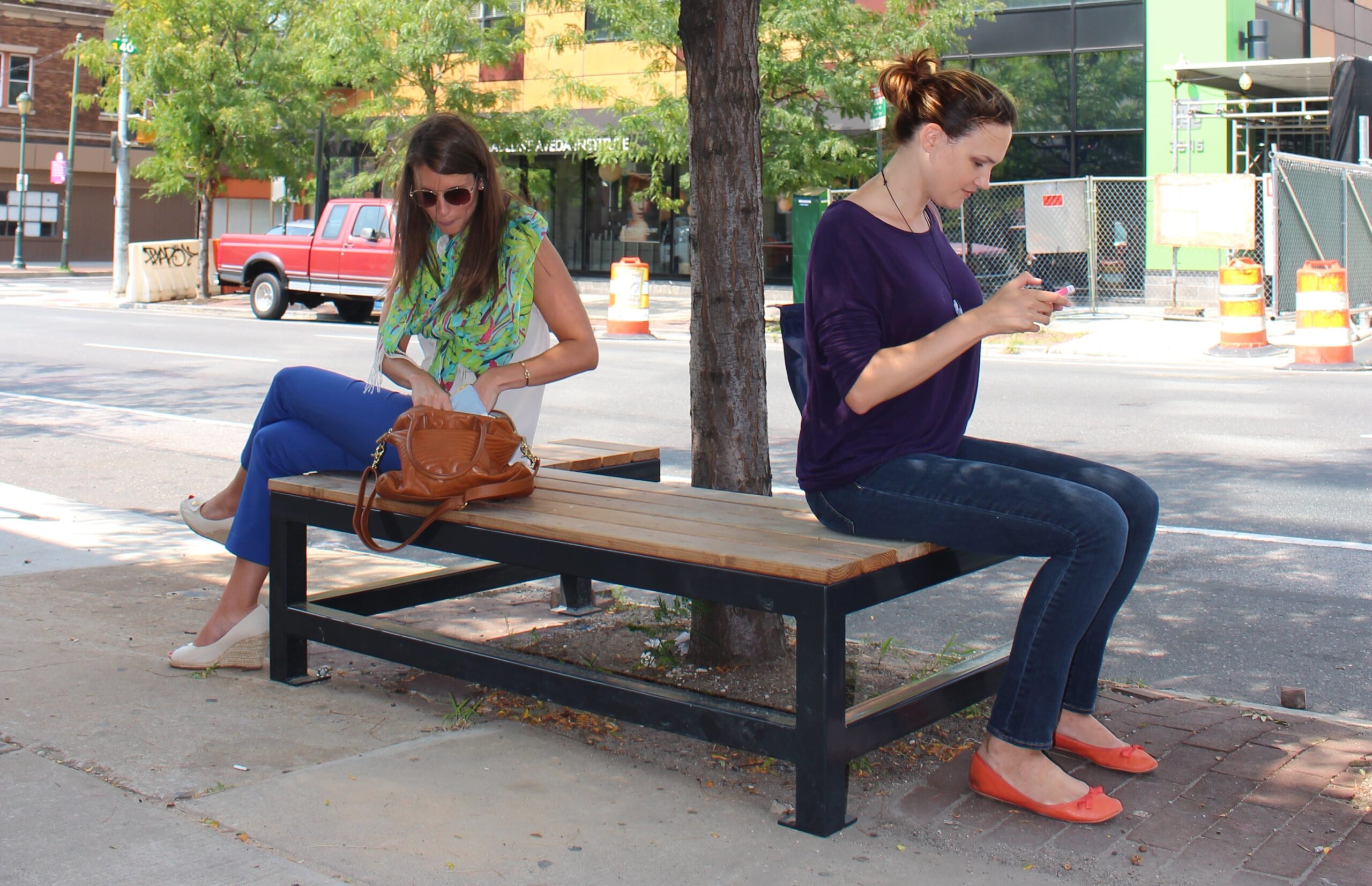 Two women sit on a University City District tree seat