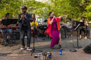 Musicians perform on stage during the Baltimore Avenue Dollar Stroll, with a singer in a bright pink dress engaging the audience.