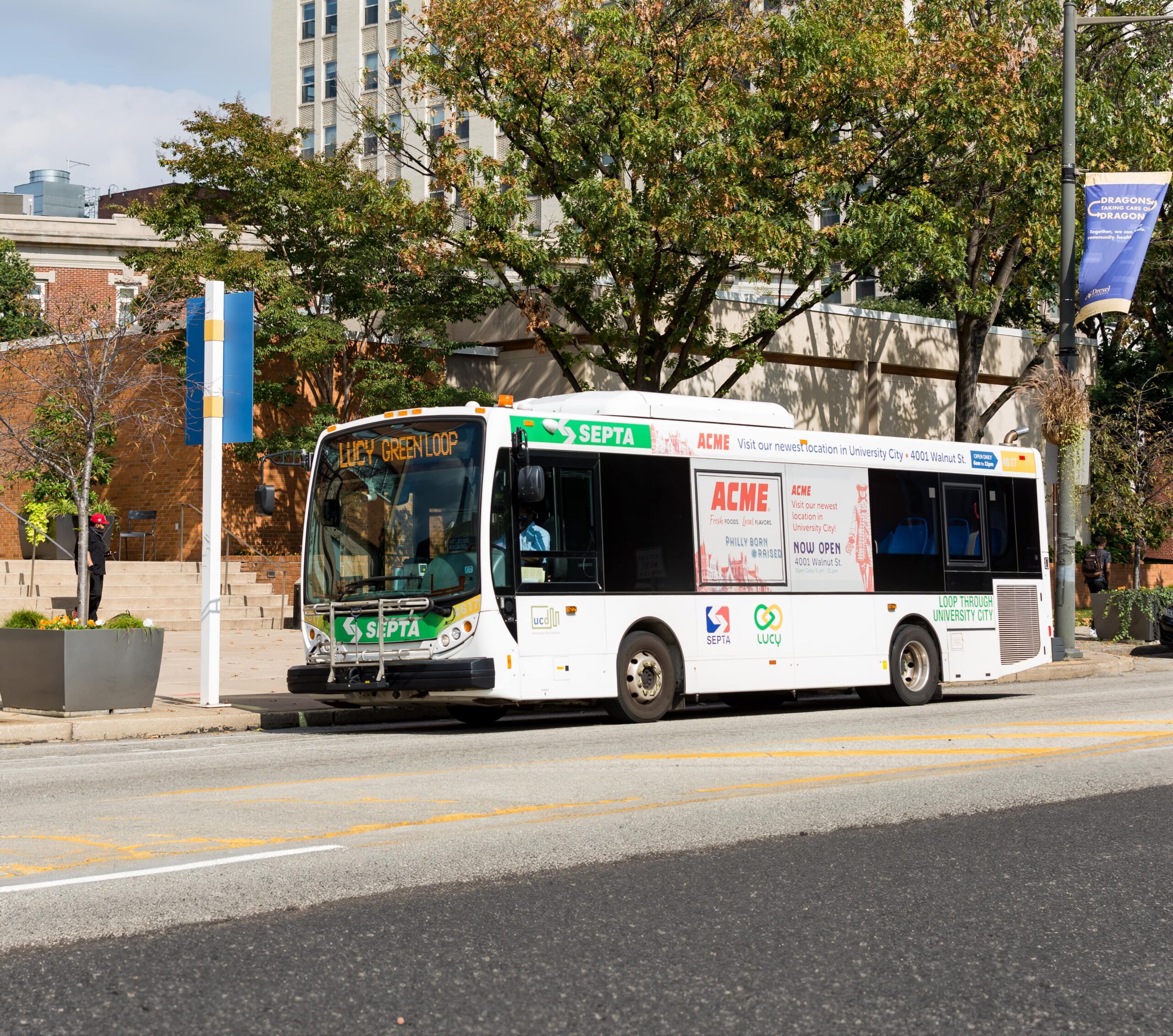 SEPTA LUCY Green Loop bus parked in University City, Philadelphia, with trees and urban architecture in the background.