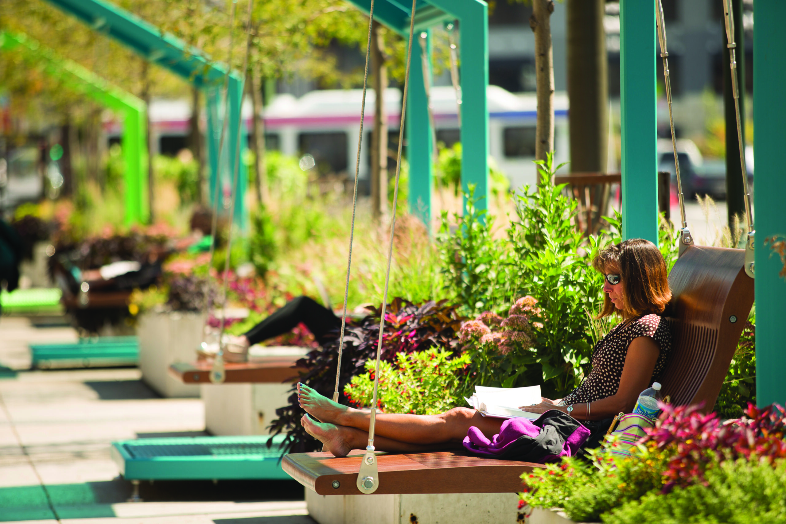 A person lounges on a swing reading, surrounded by lush greenery and vibrant flowers at The Porch at 30th Street Station.