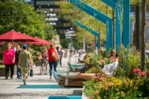 Visitors enjoy swings and greenery at The Porch at 30th Street Station, with people walking and relaxing in the vibrant public space.