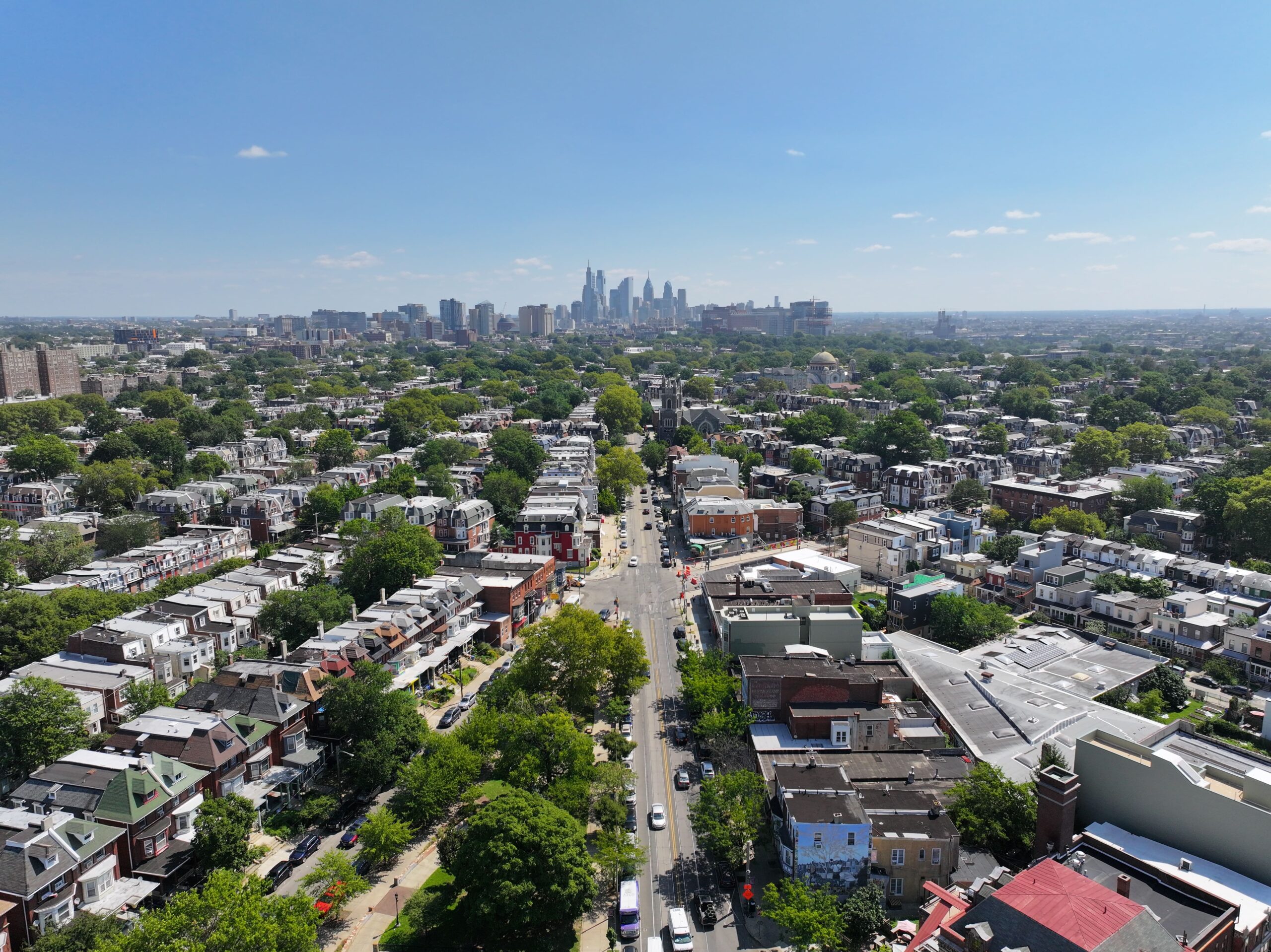 Aerial view of University City, Philadelphia, featuring tree-lined streets, historic rowhomes, and the city skyline on a clear sunny day.