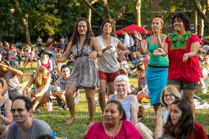 A group of people dances and smiles among a seated crowd enjoying the University City Summer Series event on a summer evening.