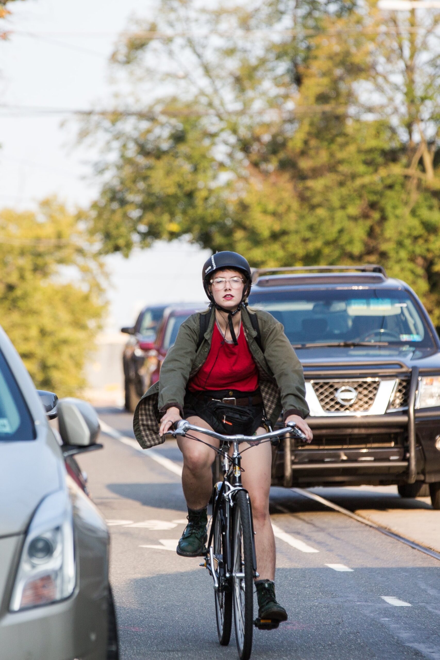 Cyclist in a red jacket riding through traffic in University City, Philadelphia, with cars and trees in the background.