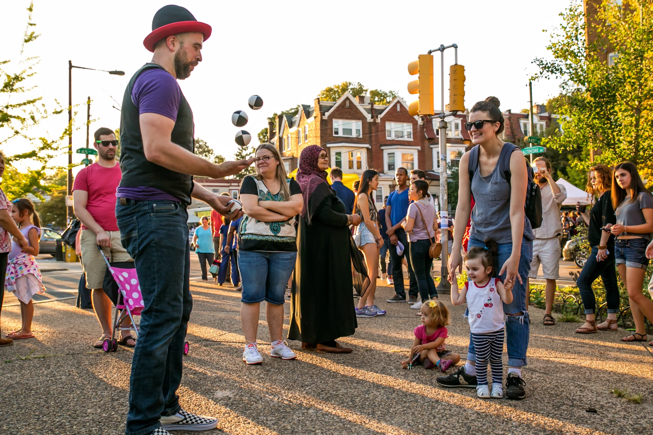 Juggler performing at Baltimore Ave Dollar stroll, surrounded by smiling onlookers