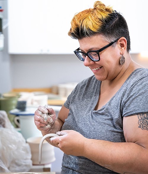 Store owner Bethany Rusen sculps a ceramic artwork, smiling.