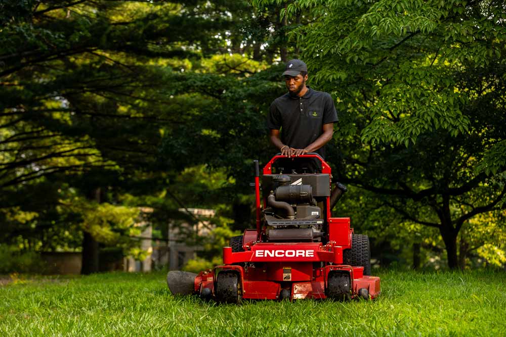 A Green City Works landscaper operating a lawnmower to maintain a large green lawn.