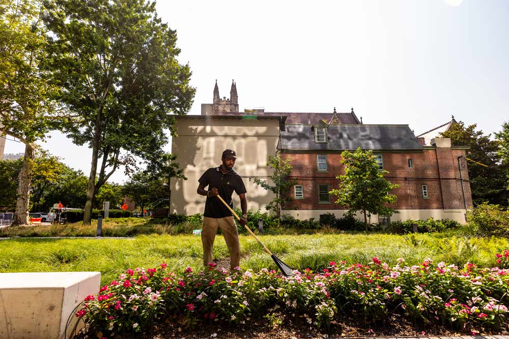 A Green City Works landscaper raking leaves to maintain a garden.