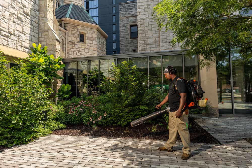 A Green City Works landscaper using a leaf blower to maintain a patio.