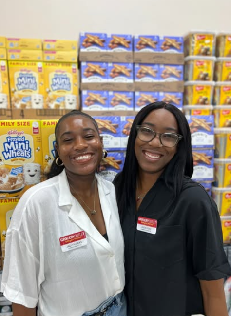 Two women, smiling in front of rows of cereal in a grocery store