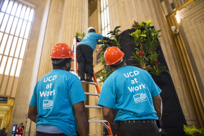 Workers installing a planter inside of 30th Street Station while wearing shirts that say "UCD at Work."