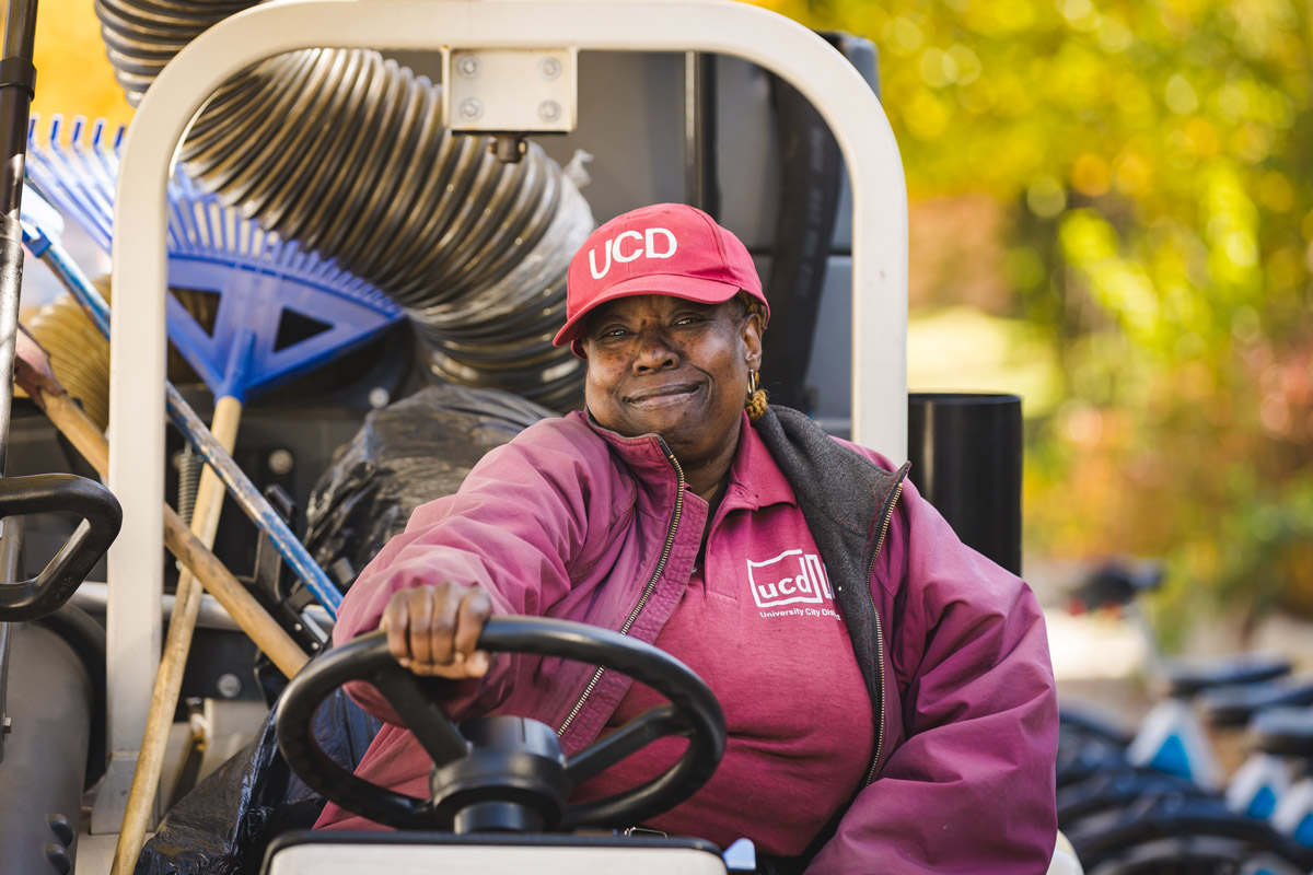 A UCD Cleaning Crew member poses behind the steering wheel of a street cleaner.