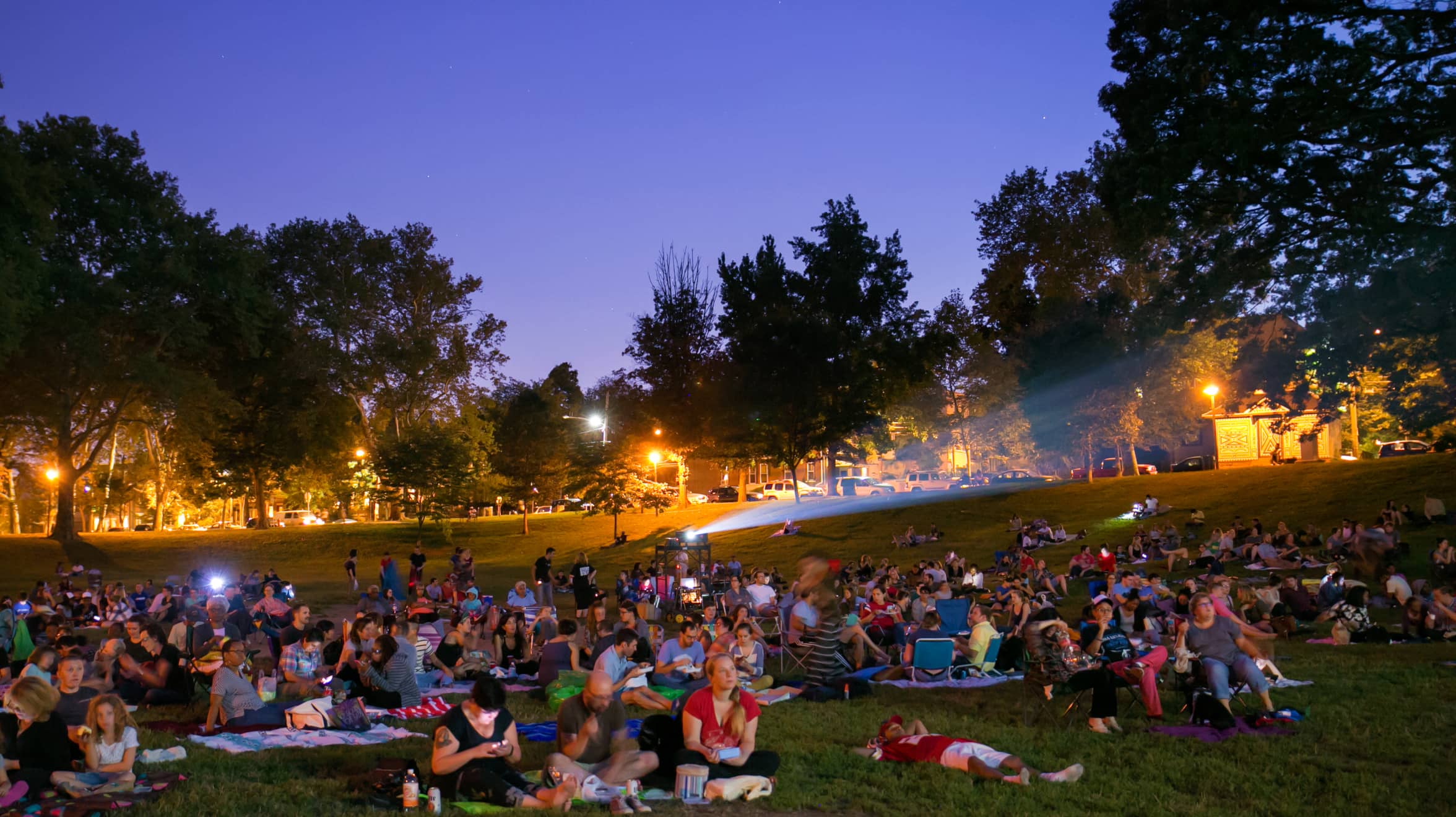 A large crowd of people sit in front of a movie screen at Movies in Clark Park