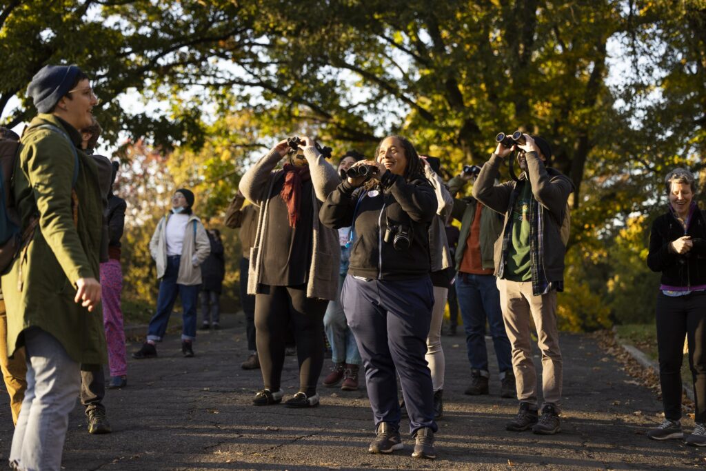 A group of bird watchers in a park look through binoculars